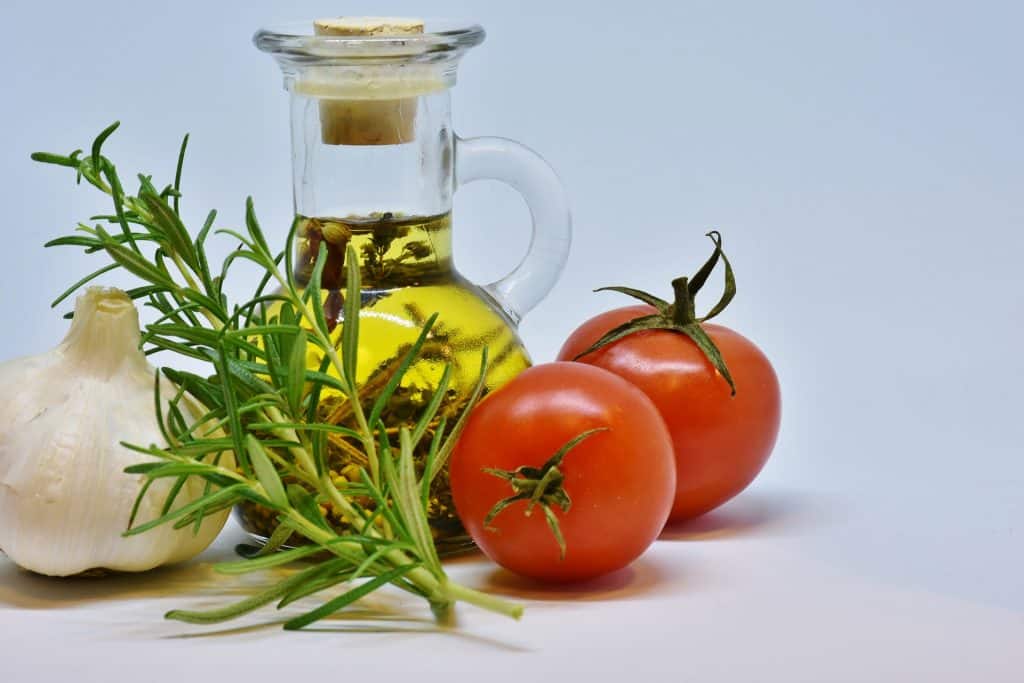 Petite bouteille d'huile d'olive entourée de deux tomates, d'une gousse d'ail et d'un aromate